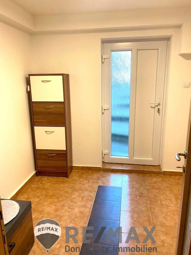 Eingangsbereich mit Fliesenboden, Schuhschrank und heller Eingangstür.