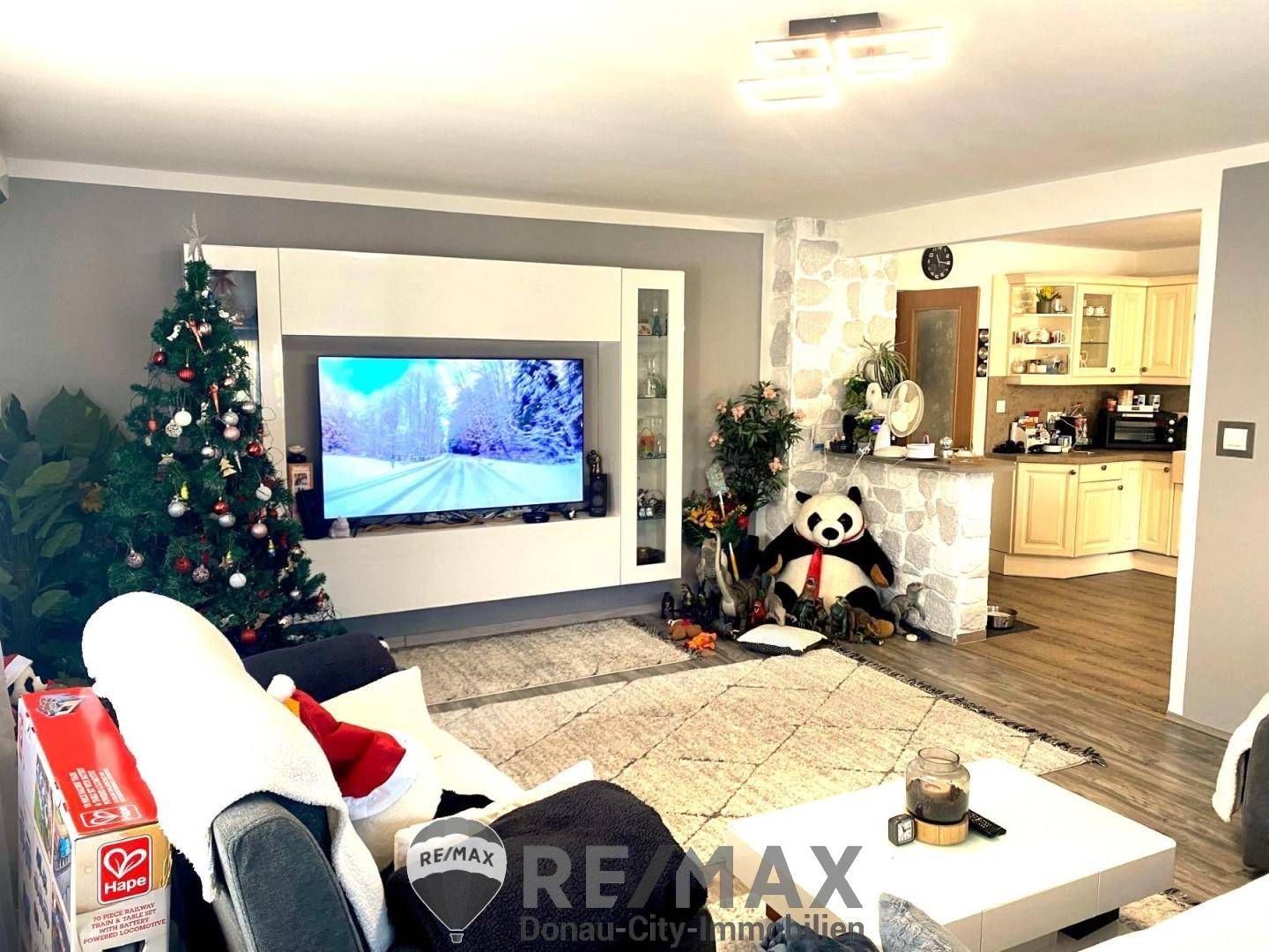 Gemütlicher Wohnbereich mit großem Fernseher, Weihnachtsbaum und Blick auf die angrenzende Küche.