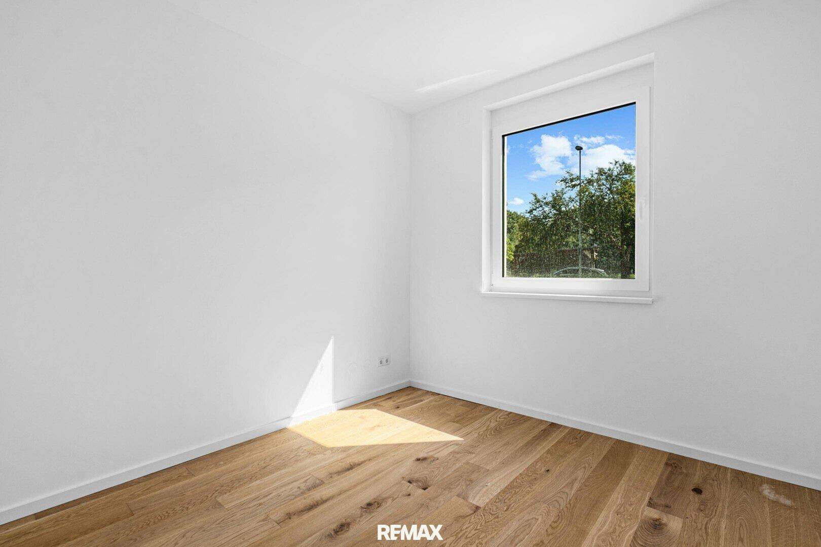 Leeres Schlafzimmer mit Eichenparkett und einem Fenster, das viel Licht hereinlässt.