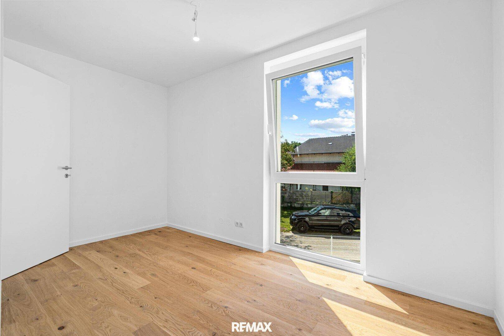 Schlafzimmer mit Holzboden und großem Fenster, das einen Blick nach draußen bietet.