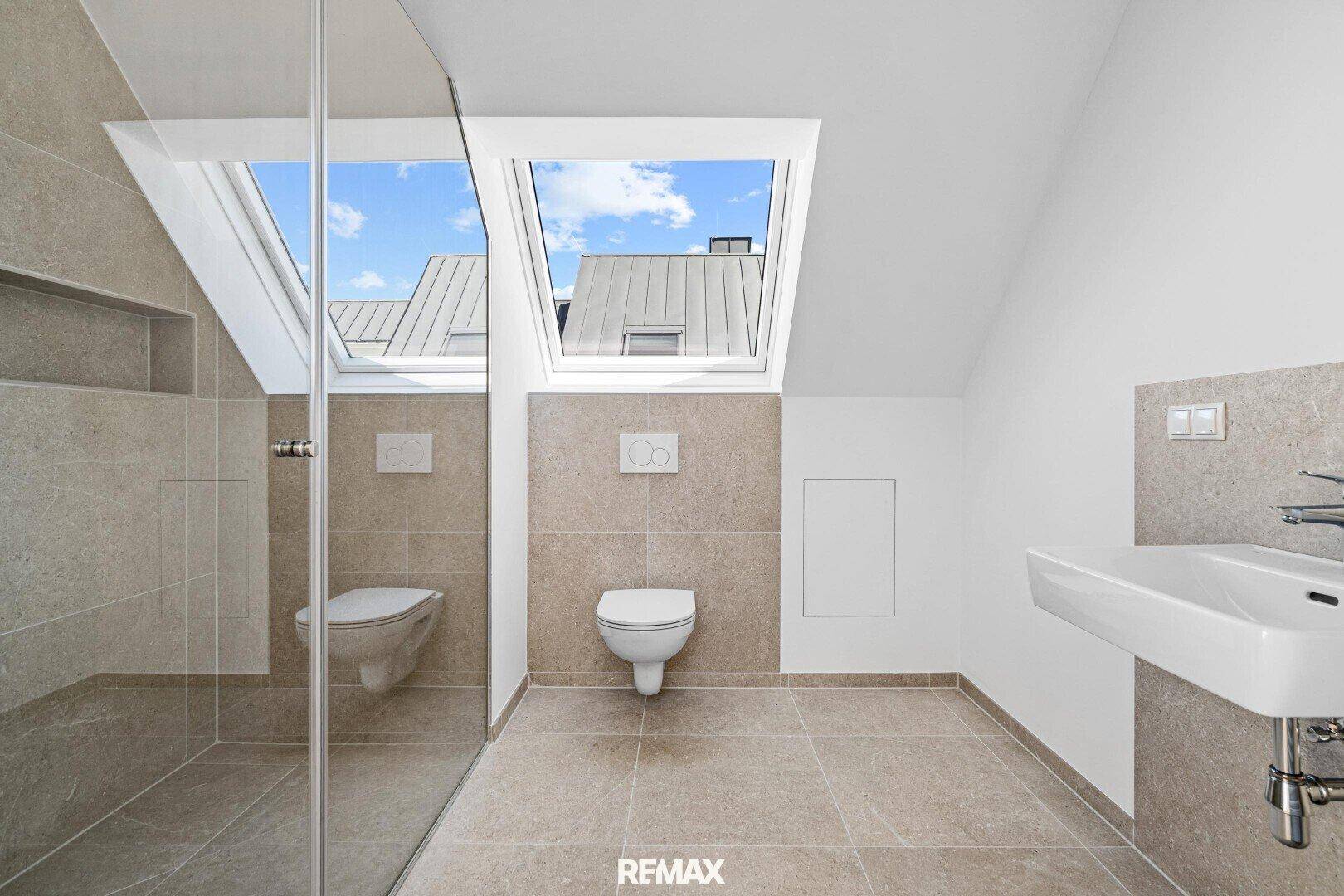 Modernes Badezimmer im Dachgeschoss mit Dusche, WC, Waschbecken und Dachfenstern.