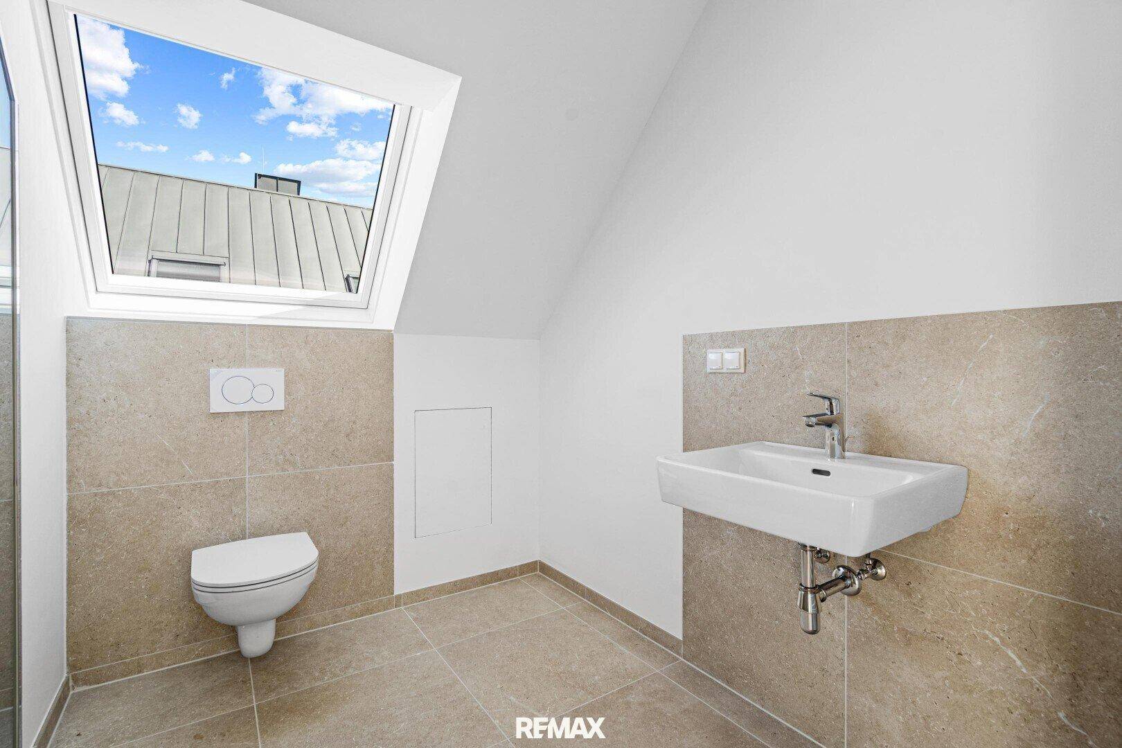 Badezimmer im Dachgeschoss mit WC, Waschbecken, beigefarbenen Fliesen und Dachfenster.