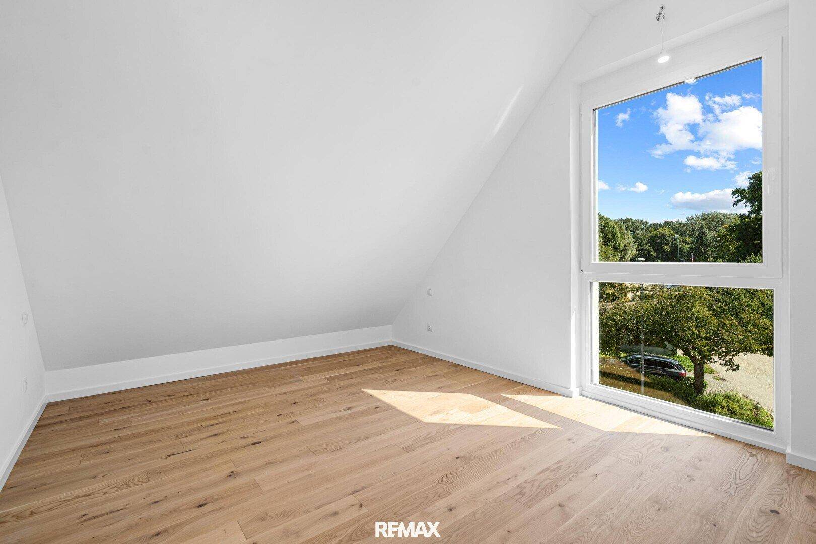 Dachgeschoss-Schlafzimmer mit schräger Decke, Parkettboden und großem Fenster.