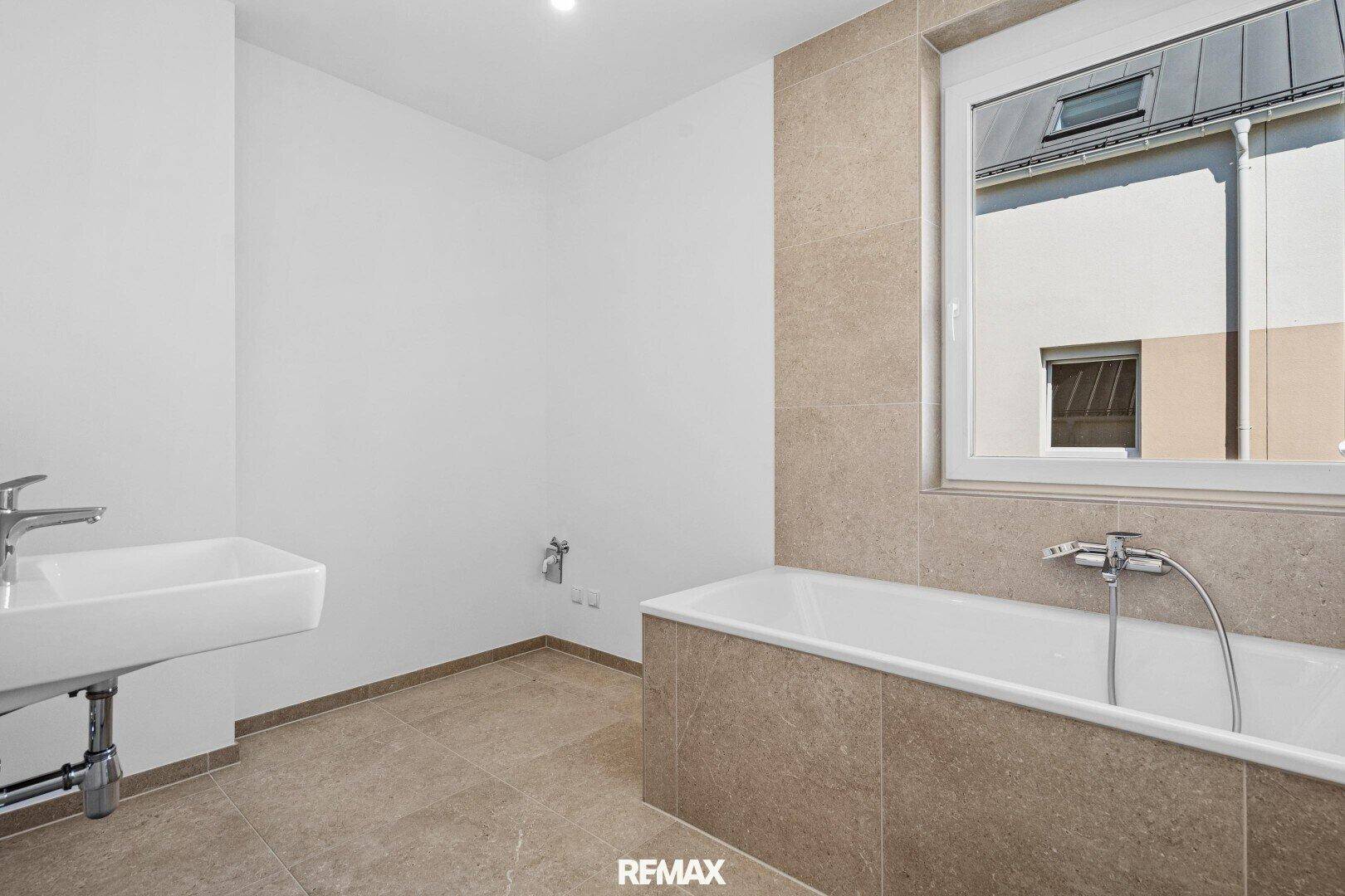 Badezimmer mit Badewanne, modernem Waschbecken und beigefarbenen Wandfliesen.