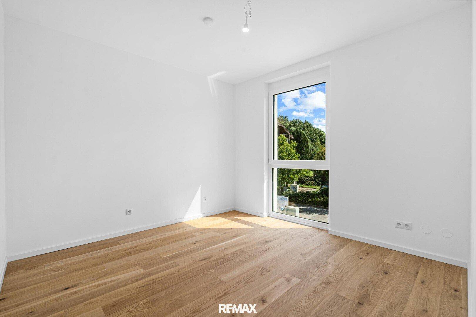 Geräumiges Schlafzimmer mit hellem Parkettboden und großem Fenster für viel Tageslicht.