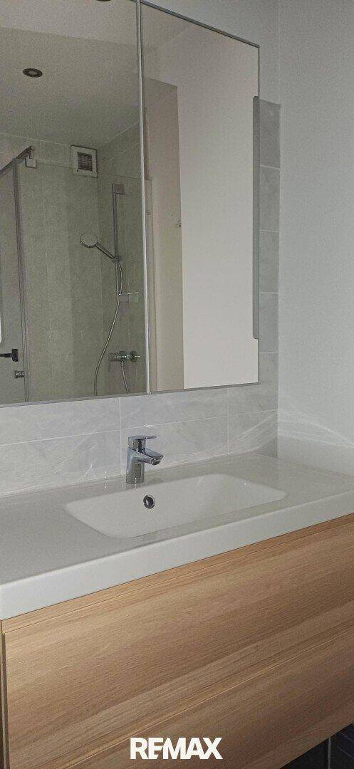 Modernes Badezimmer mit Einzelwaschbecken, großem Spiegelschrank und Duschbereich.