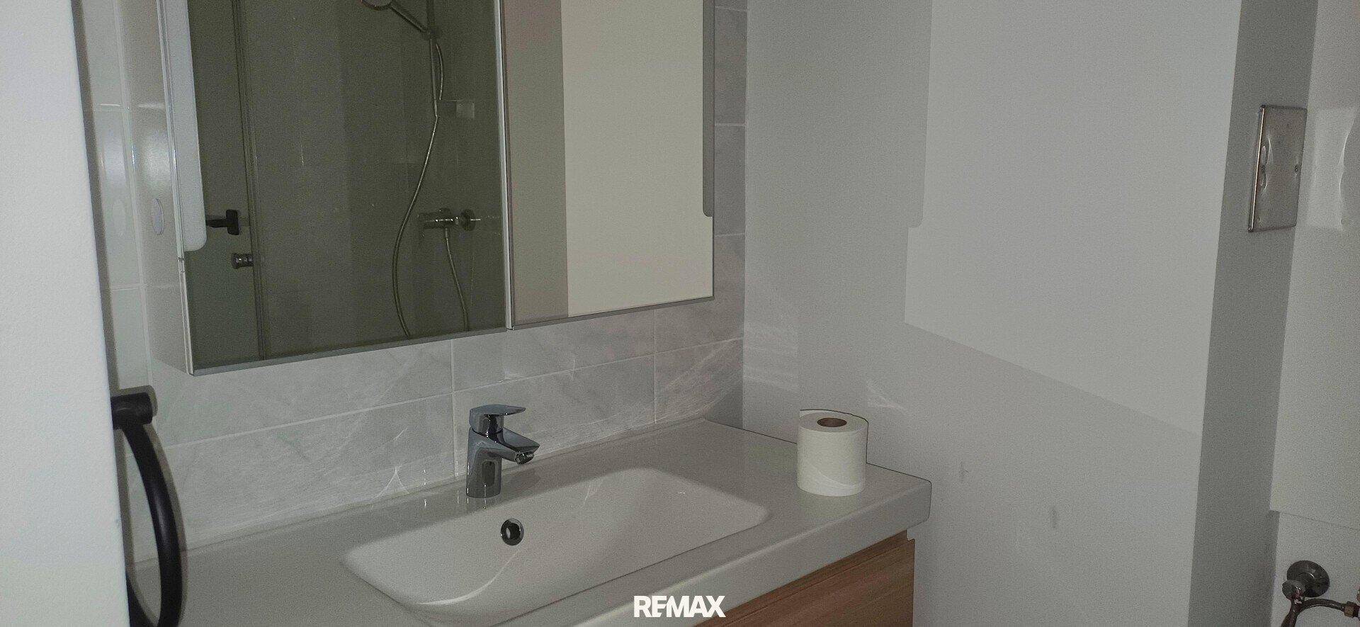 Helles Badezimmer mit modernem Waschbecken, Spiegel und praktischer Ablagefläche.