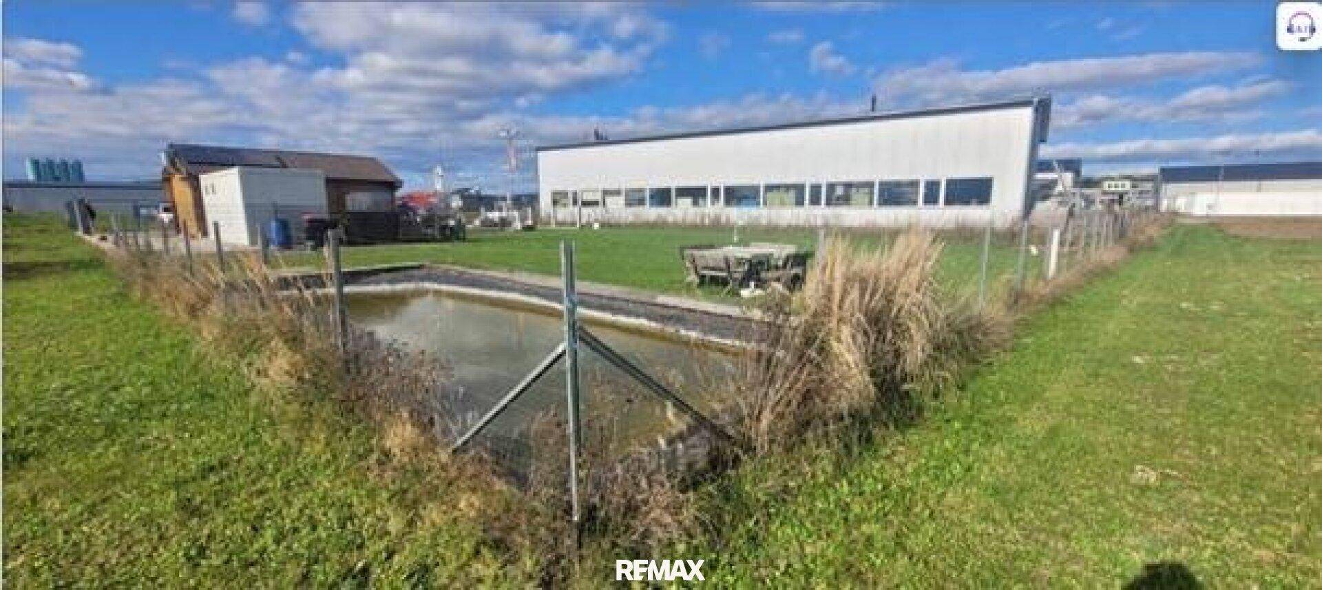 Weitläufiges Grundstück mit einem Teich, Rasenfläche und einem Imbissgebäude im Hintergrund.