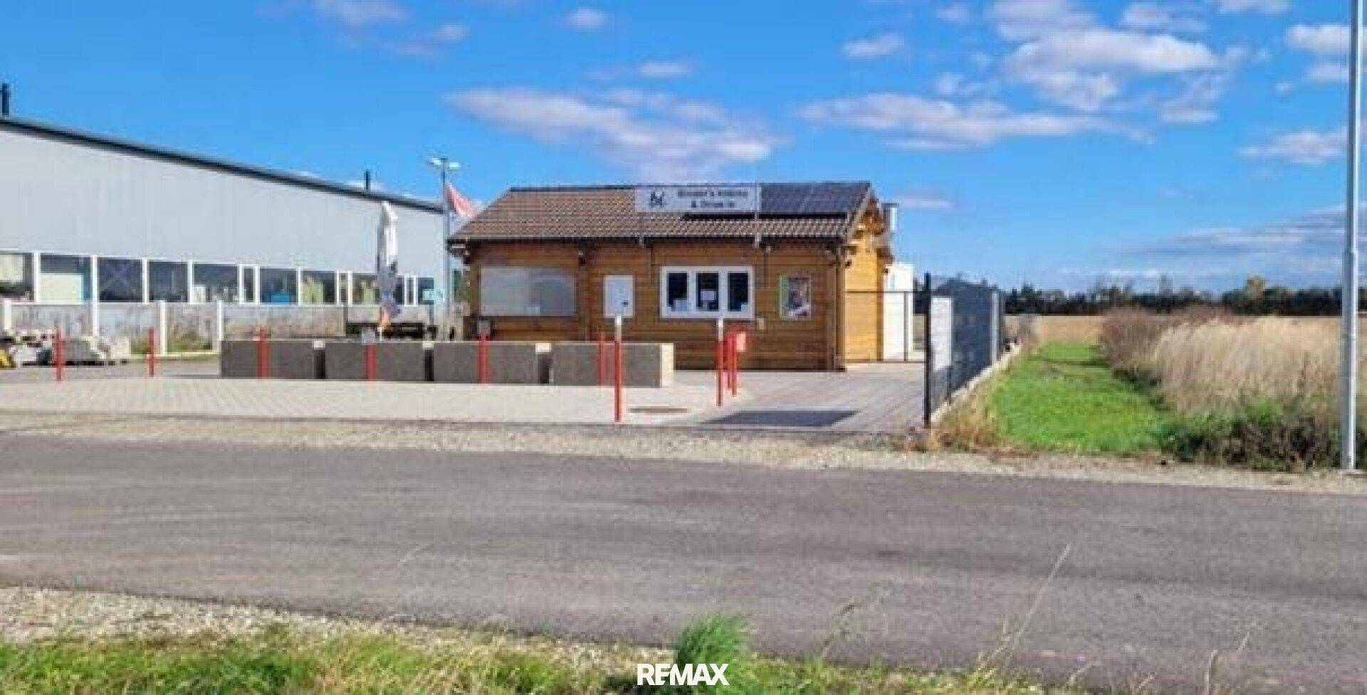 Holzgebäude mit Solarpaneelen auf dem Dach, umgeben von Feldern und einem größeren Gebäude.