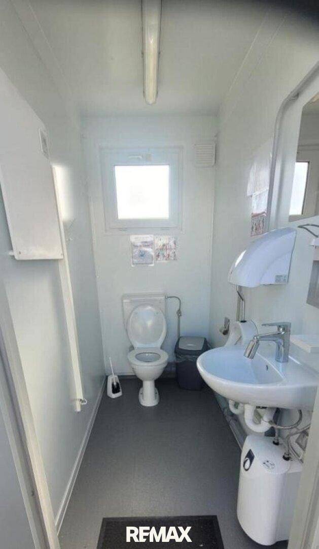 Einfache Toilette mit Waschbecken, Fenster und hellen Wänden.
