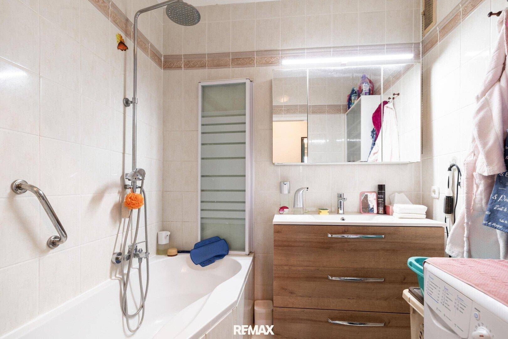 Badezimmer mit Badewanne, Dusche, Waschtisch und hellen Fliesen.