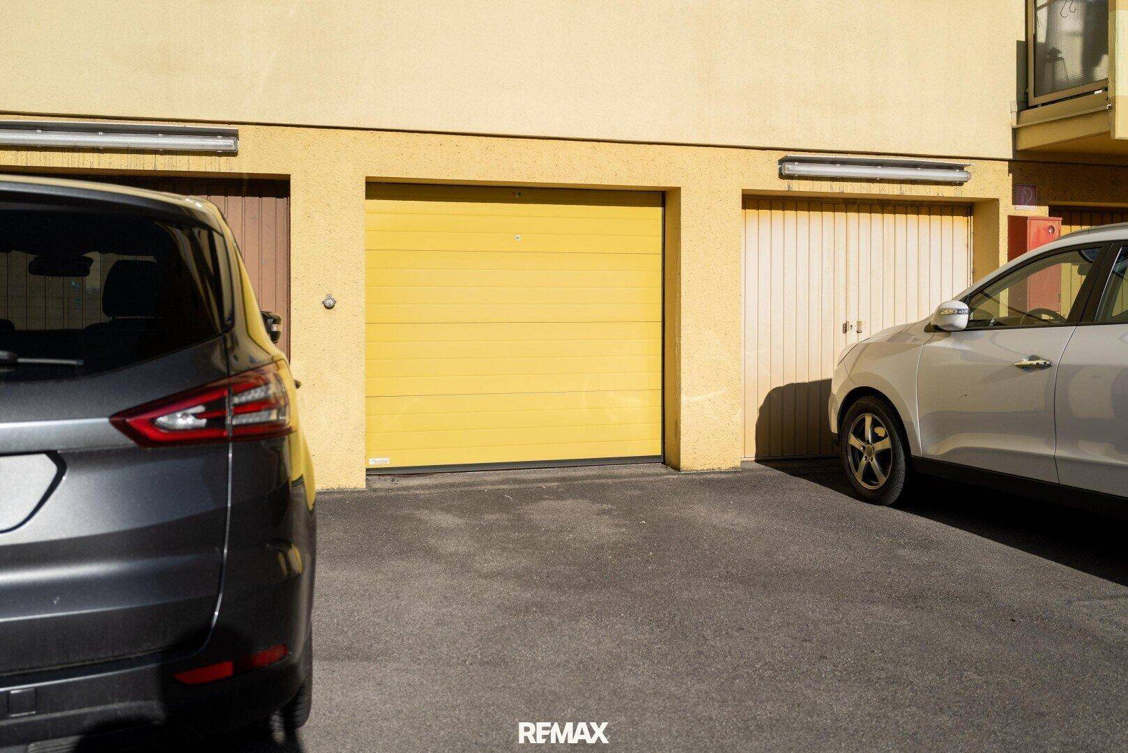 Garagenreihe mit gelben Toren und parkenden Autos davor.