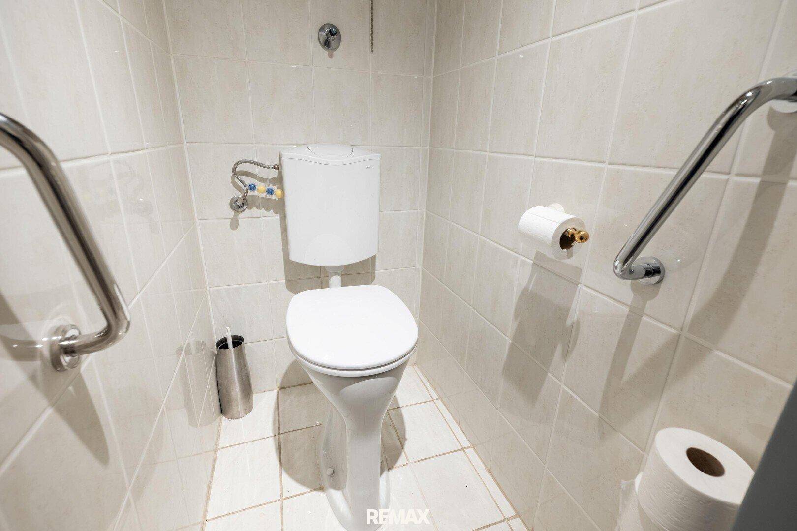 Separate Toilette mit Wand-WC, Fliesen und Haltegriffen.