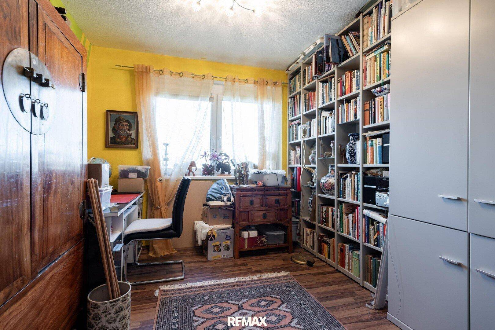 Arbeitszimmer mit Bücherregal, Schreibtisch und gelben Wänden.