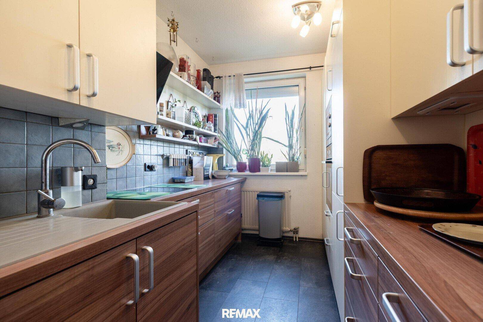 Helle Küche mit Fenster, Holzfronten und Fliesenboden.