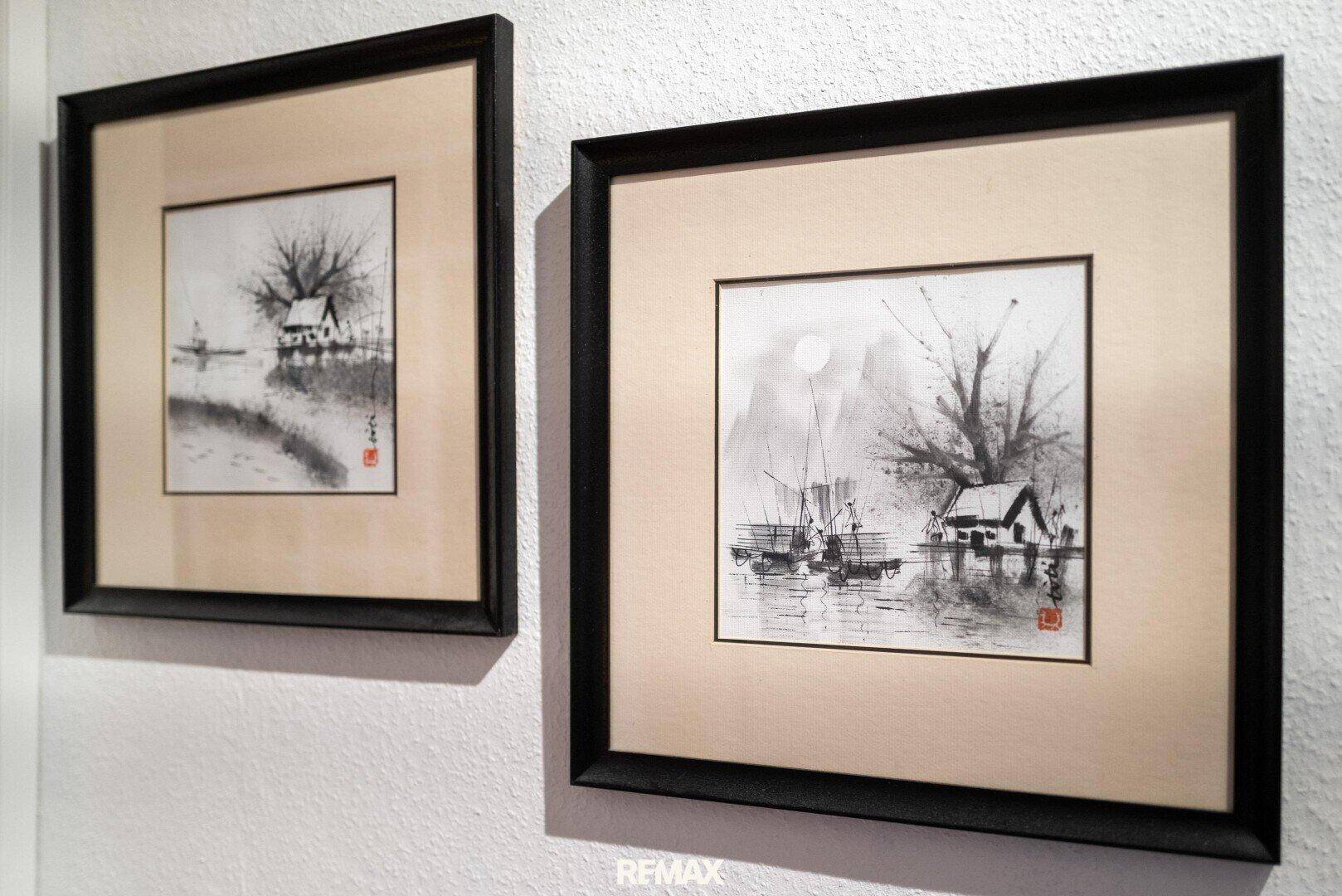 Nahaufnahme von zwei gerahmten Kunstwerken an einer weißen Wand.