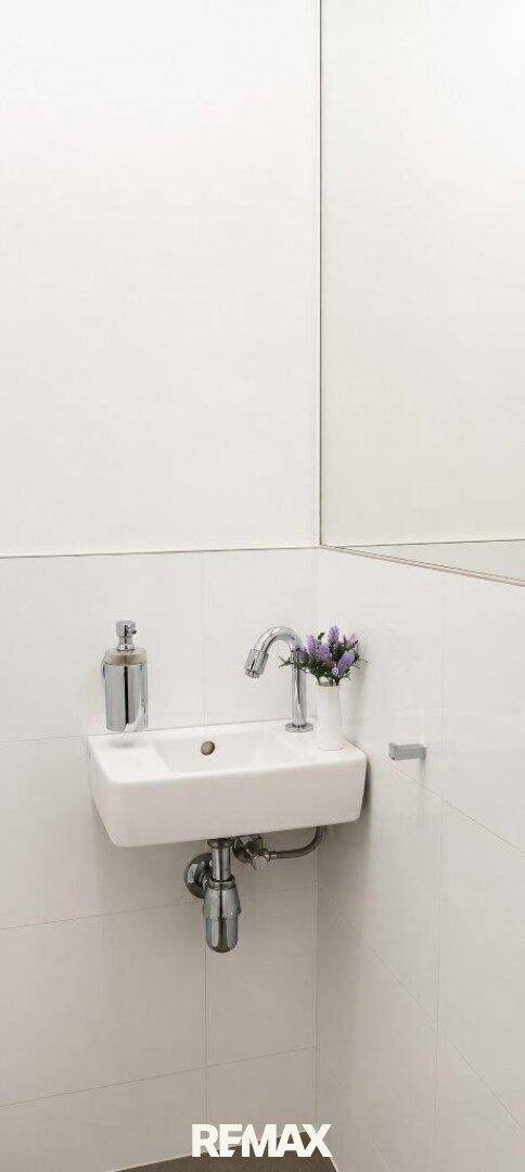 Kleines WC mit wandmontiertem Waschbecken und großem Spiegel.