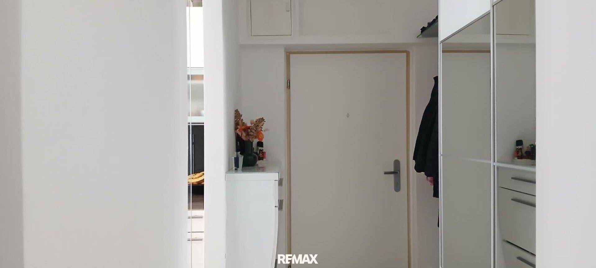 Heller Eingangsbereich mit weißer Tür, kleinem Schrank und Spiegelschrank.