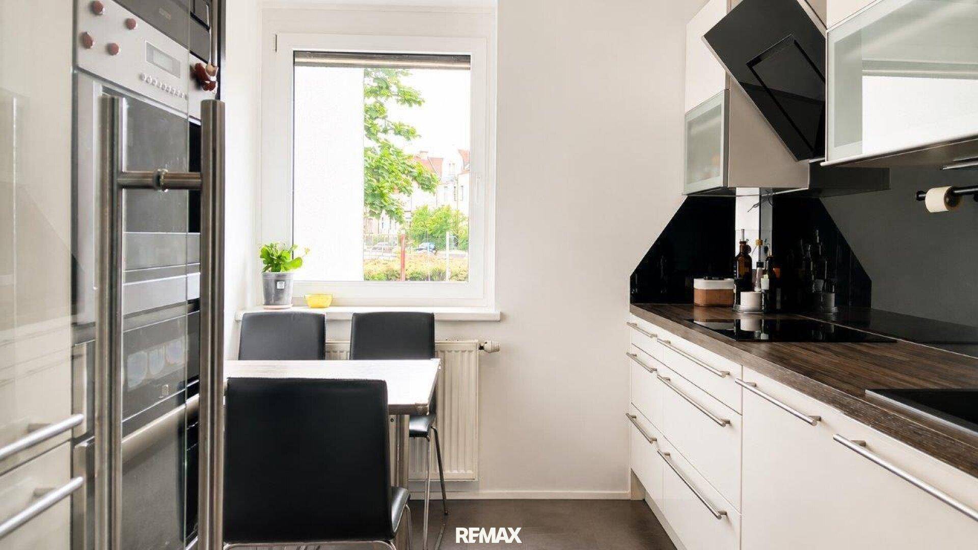 Moderne Küche mit weißen Schränken, dunkler Arbeitsplatte und Essbereich am Fenster.