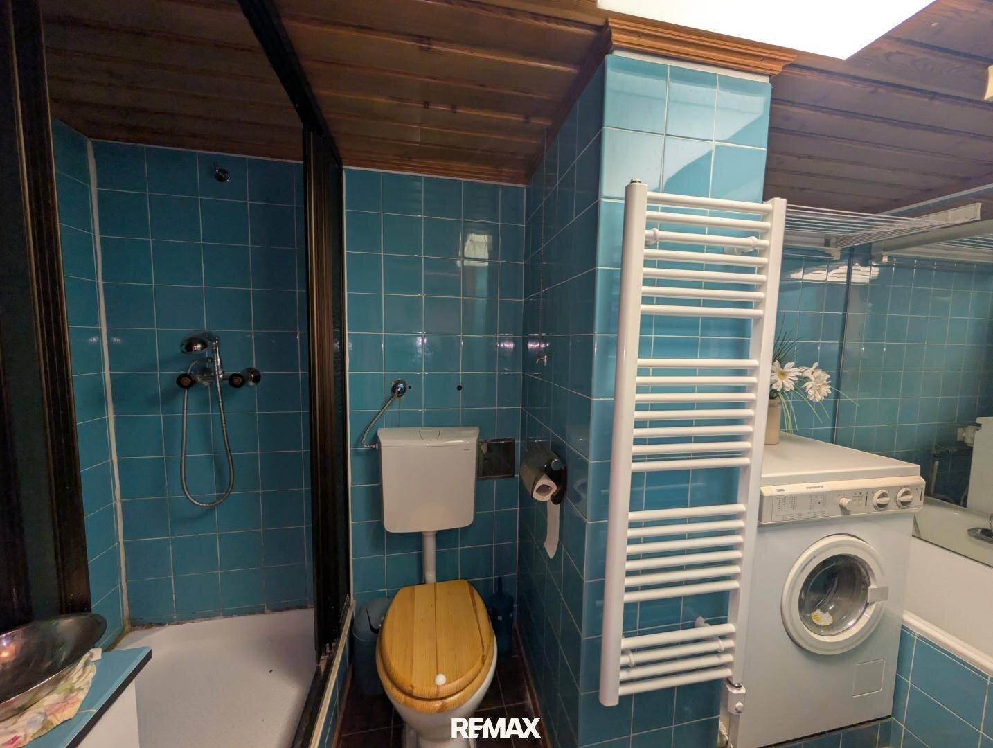 Badezimmer mit blauen Fliesen, Dusche, WC und Waschmaschine.
