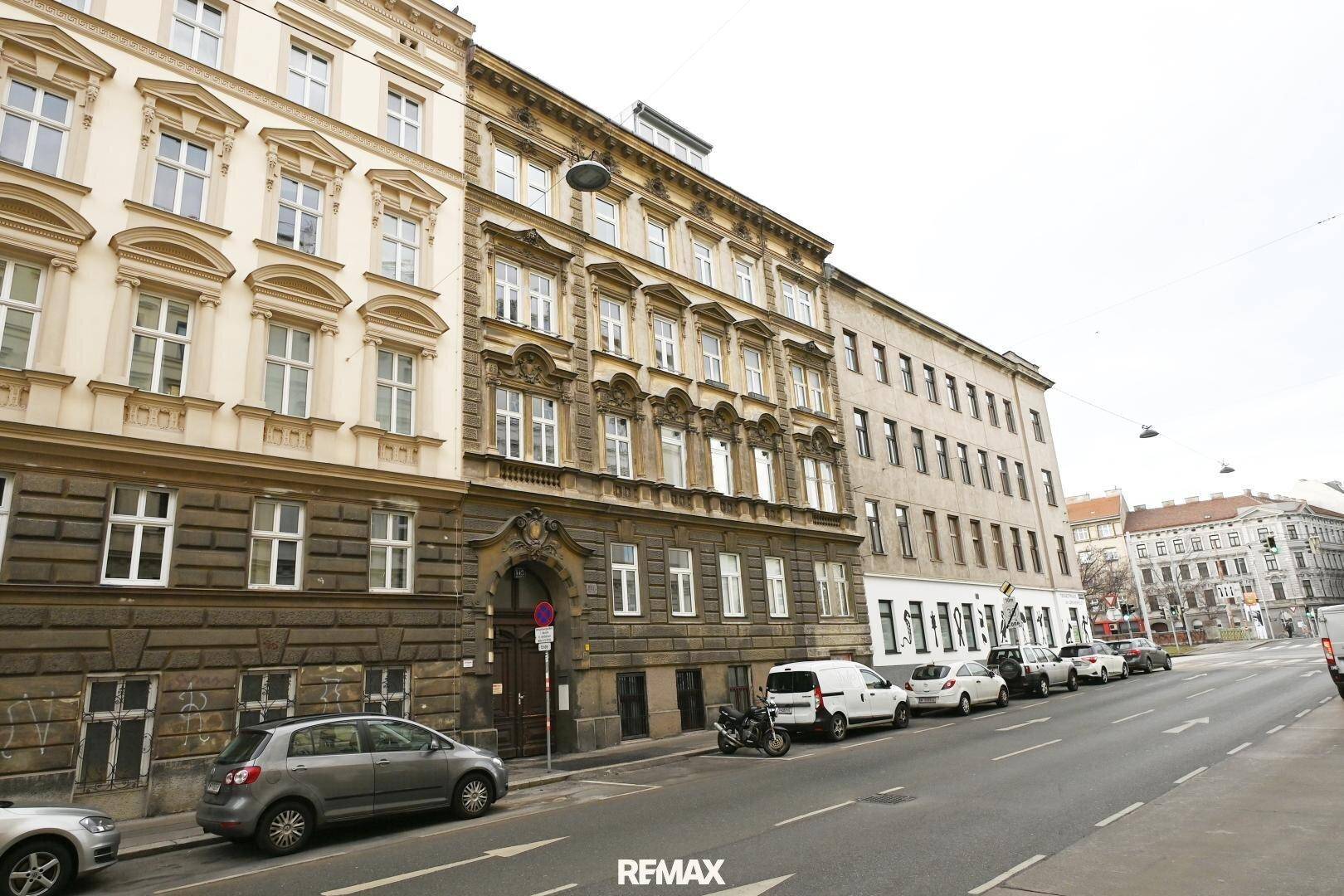 Historische Gebäude an einer belebten Straße mit parkenden Autos.