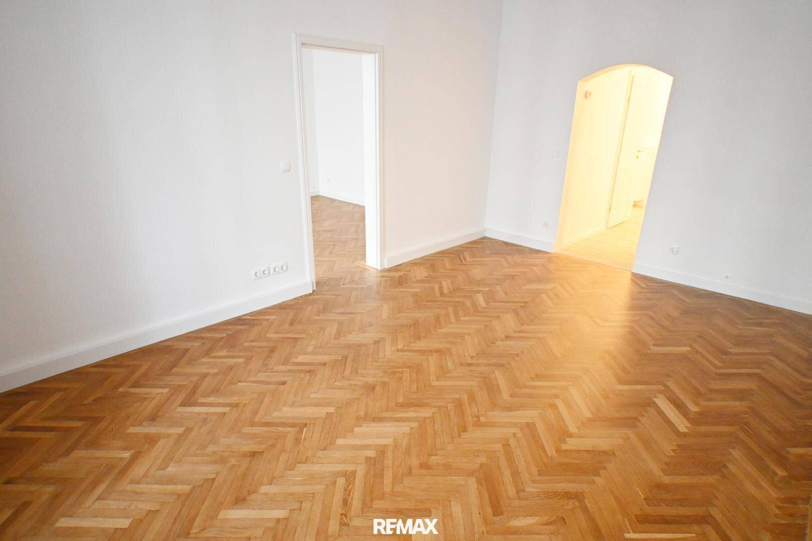 Geräumiges Zimmer mit Fischgrätparkett und Zugang zu einem weiteren Raum.
