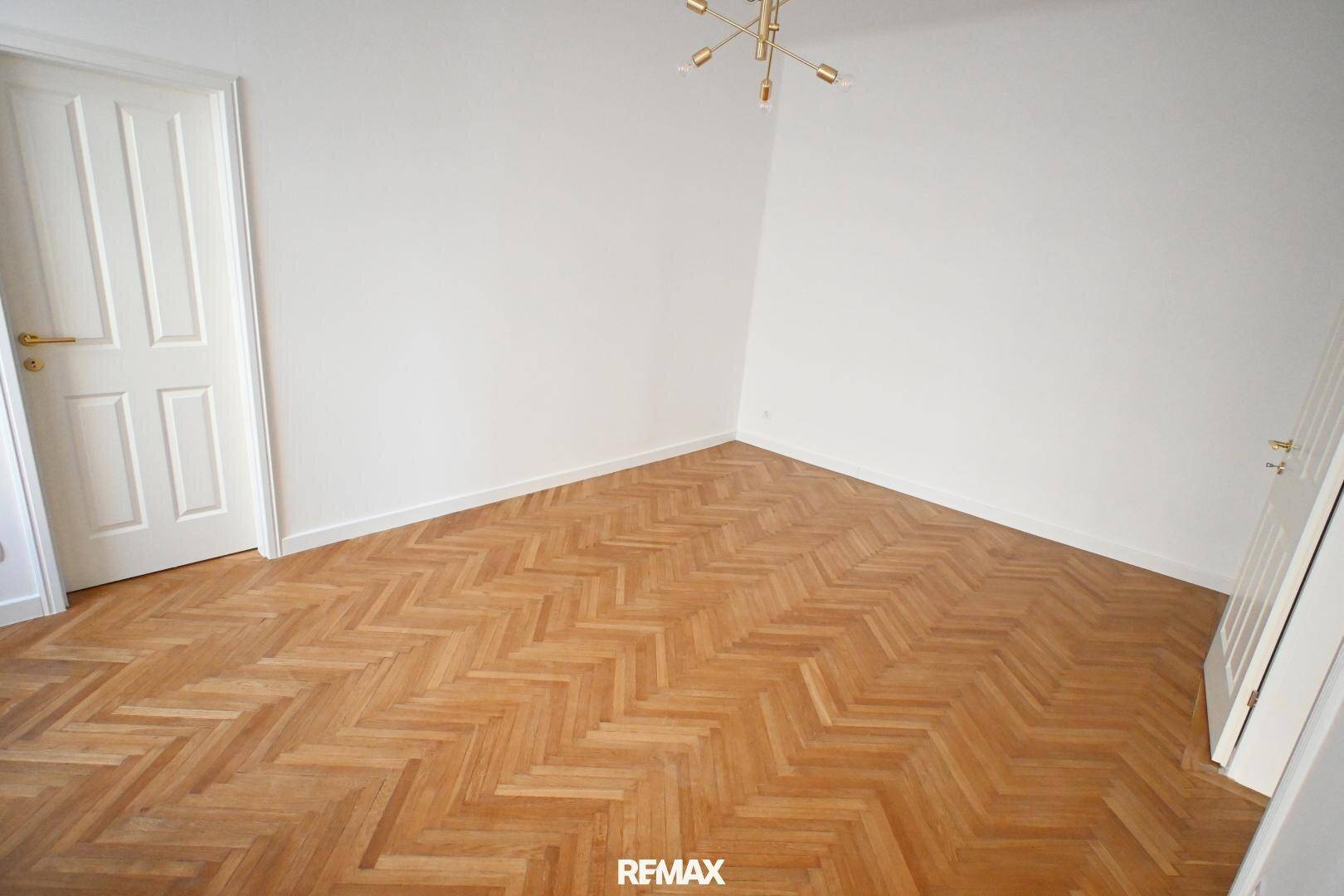 Heller Raum mit Fischgrätparkett, weißen Wänden und einer modernen Deckenleuchte.