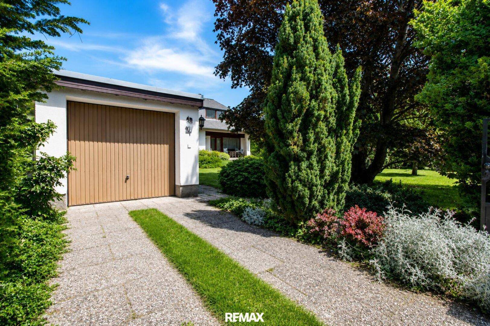 Einfahrt zur Garage mit gepflastertem Weg und grüner Bepflanzung.