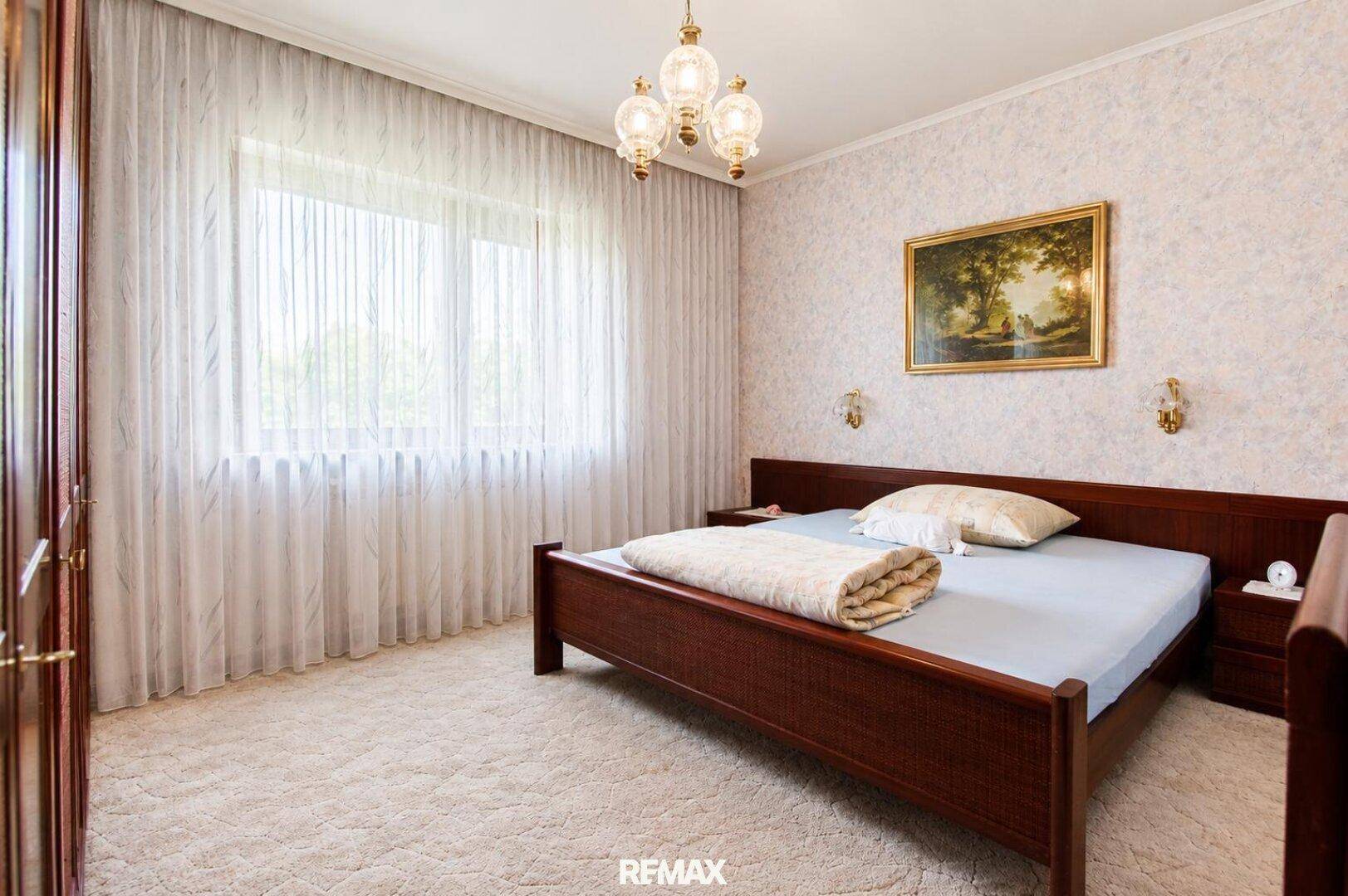 Helles Schlafzimmer mit Teppichboden, großem Fenster und klassischem Holzbett.