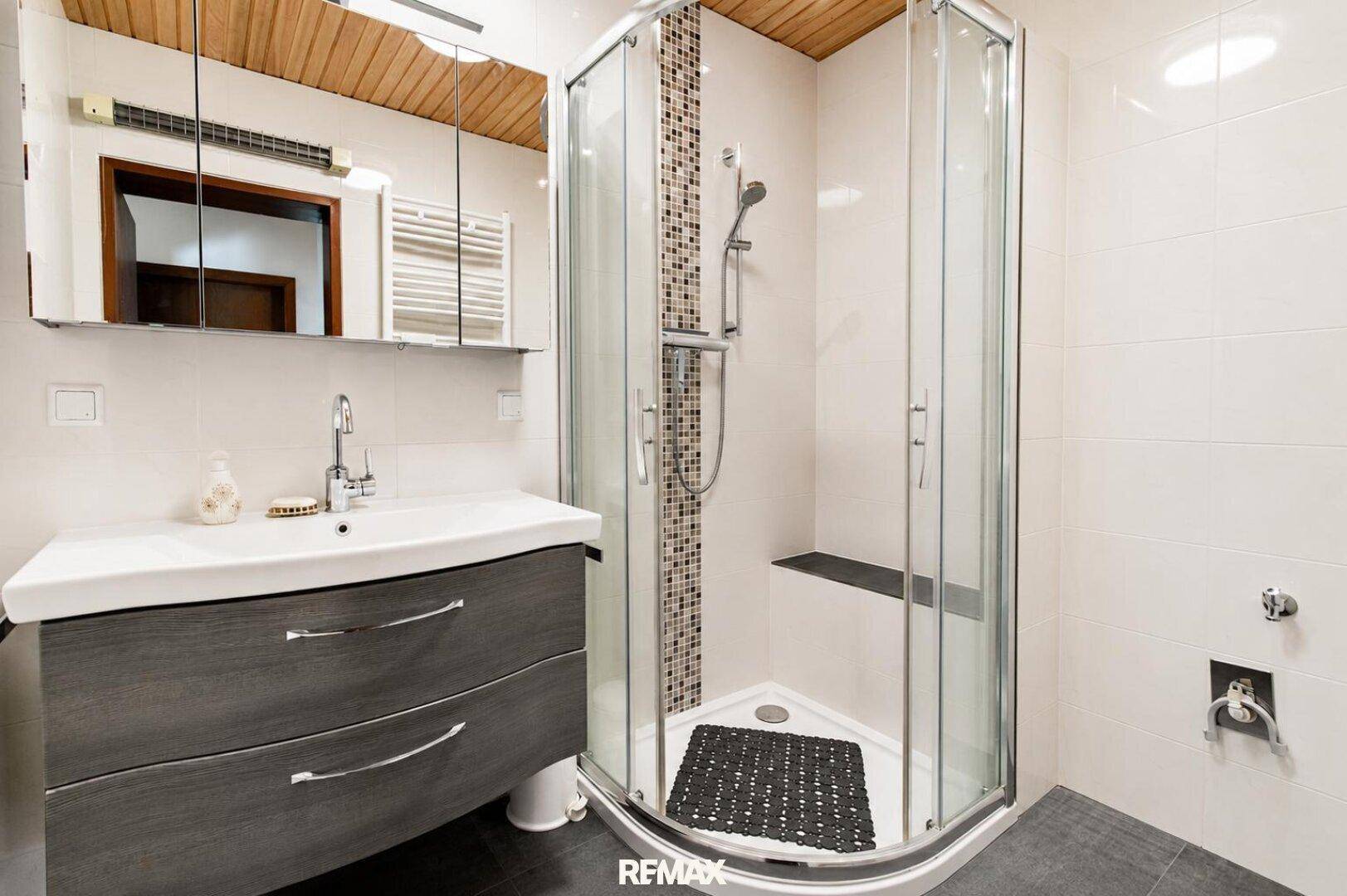 Modernisiertes Badezimmer mit Duschkabine, Waschtisch und Holzpaneeldecke.