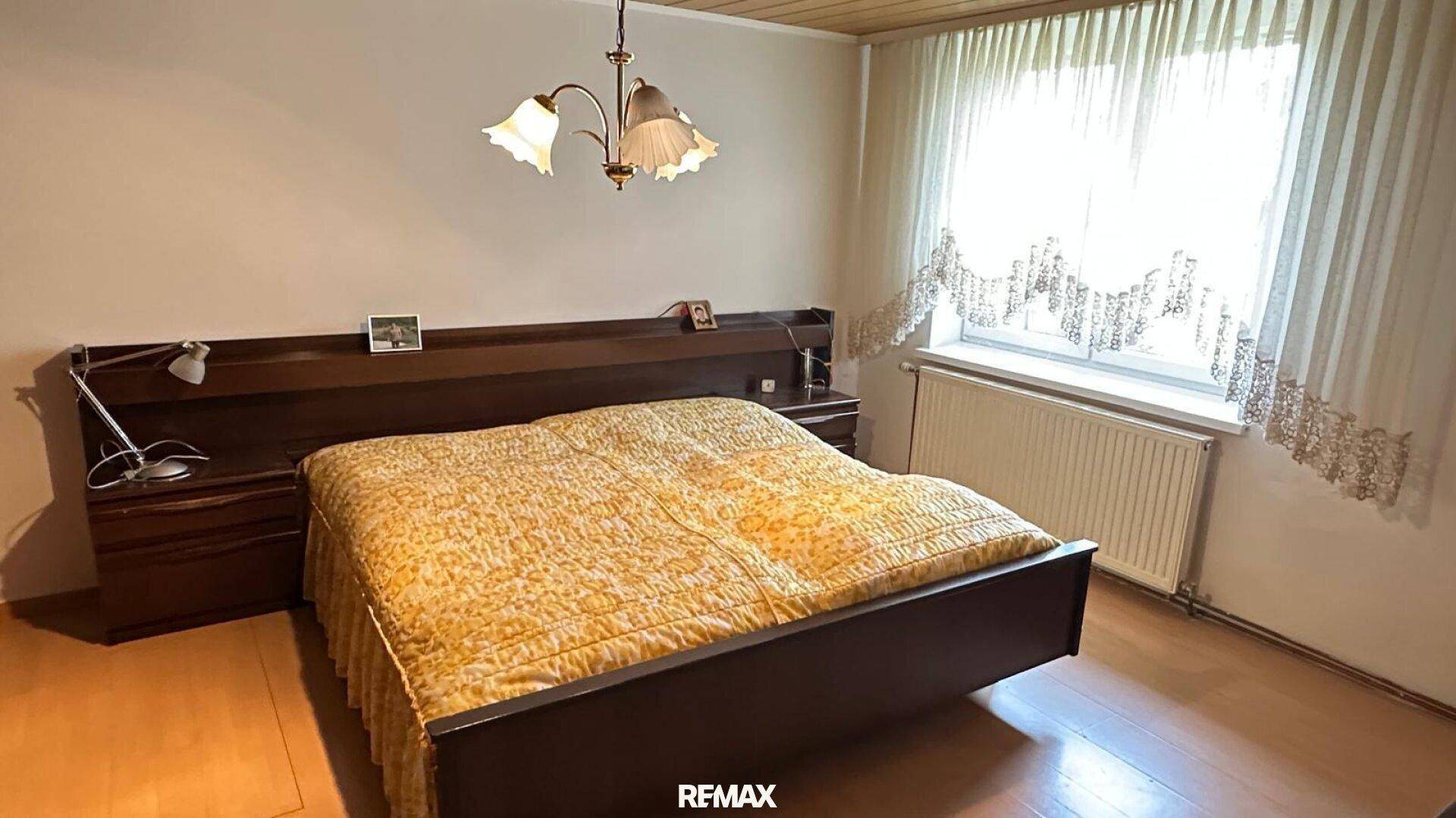 Schlafzimmer mit Doppelbett, Nachttischen und Fenster mit Vorhängen.
