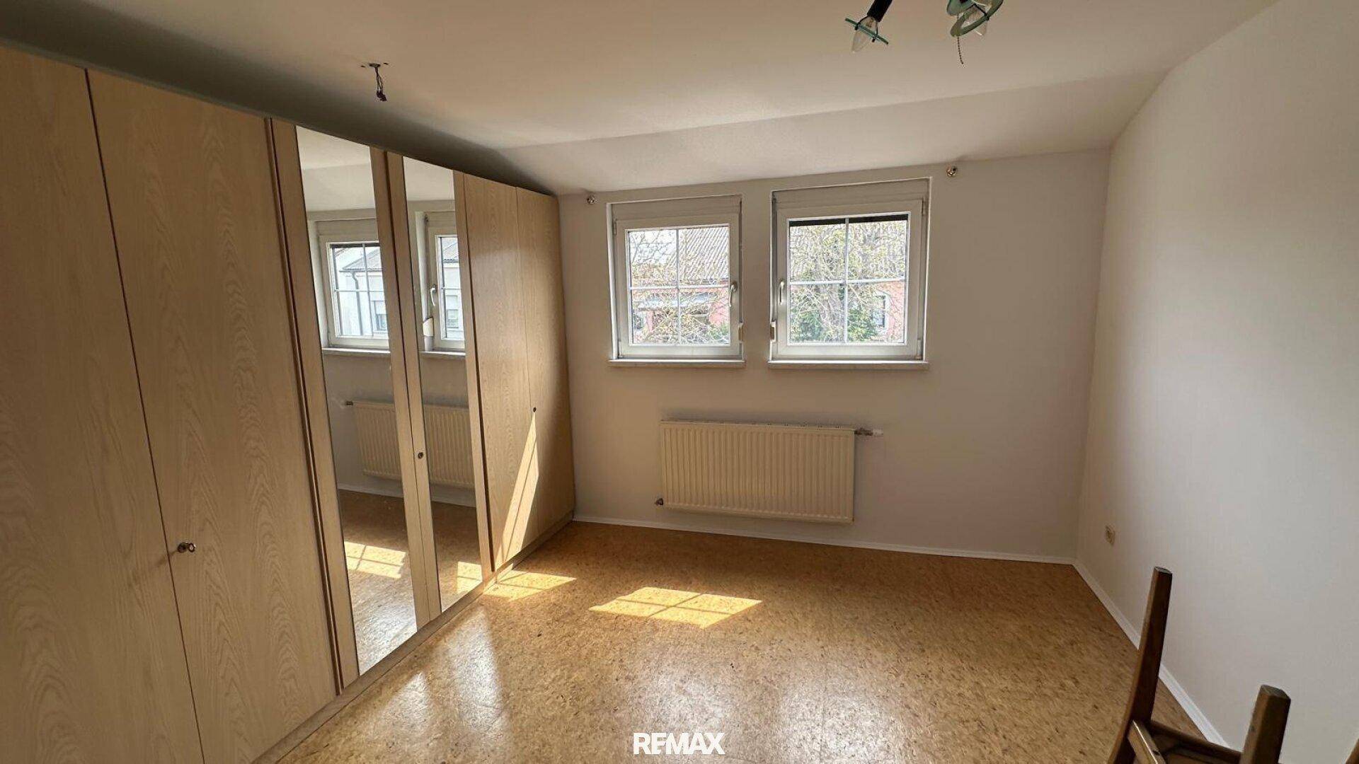 Schlafzimmer mit Spiegelschränken, Korkboden und viel Tageslicht.