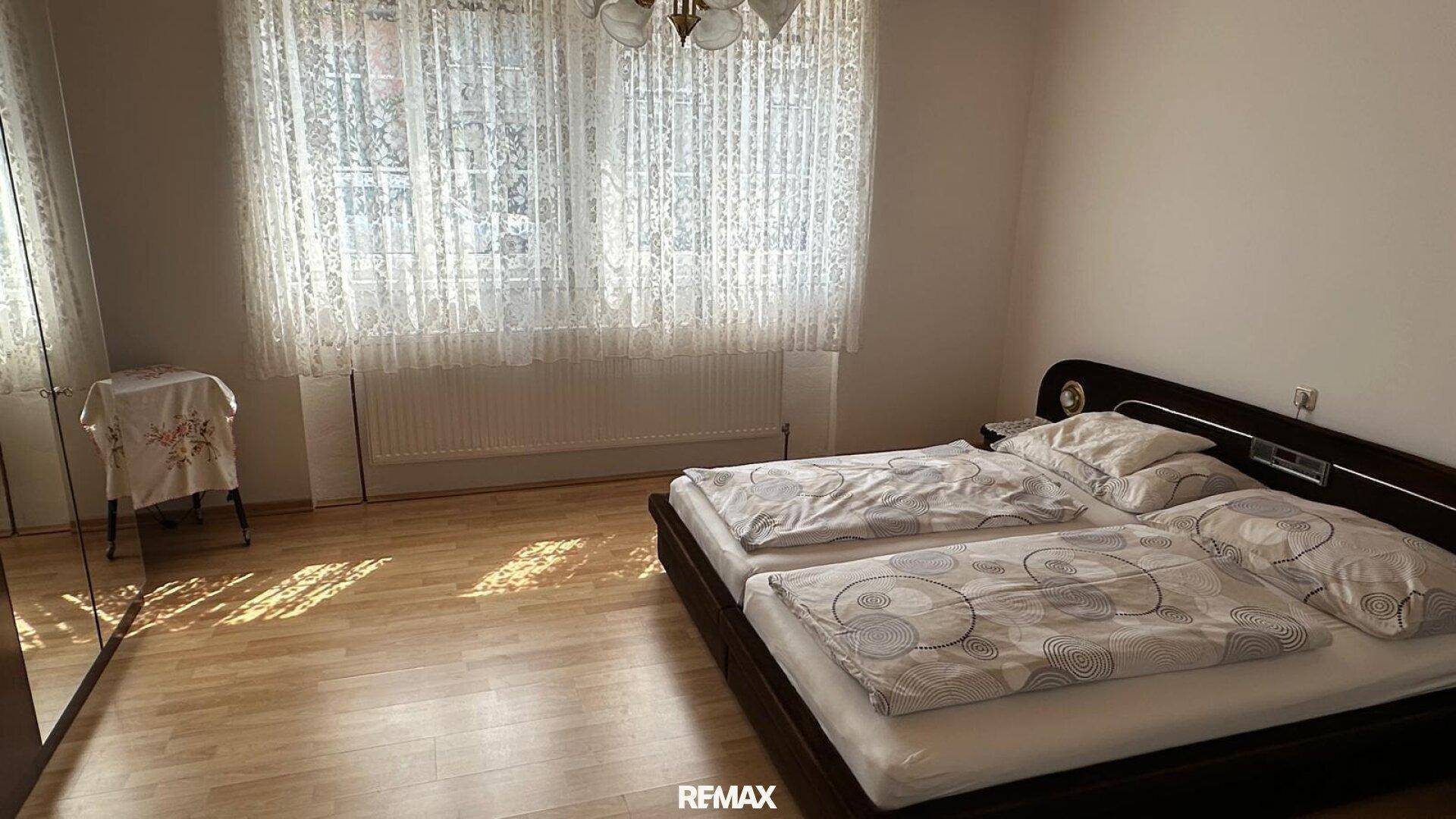Schlafzimmer mit Doppelbett, Holzboden und großen Fenstern für viel Licht.