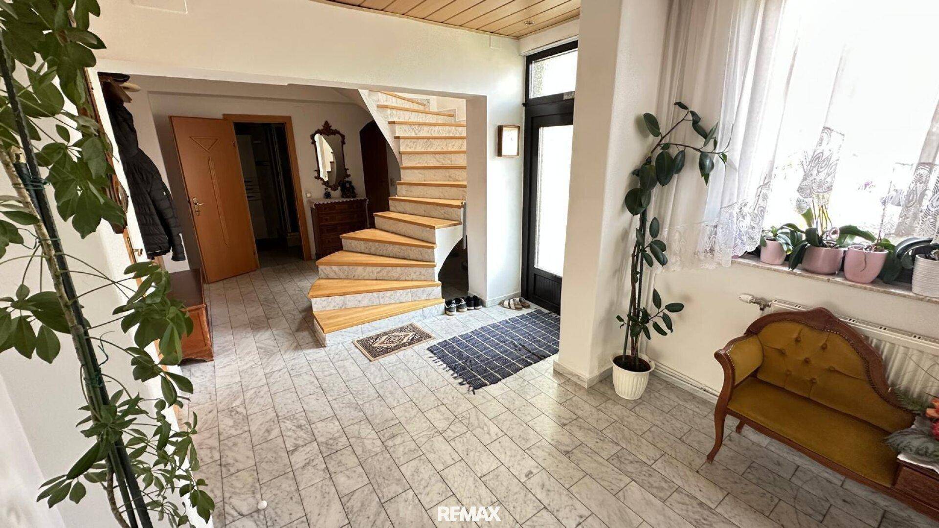 Geräumiger Eingangsbereich mit Holztreppe, Fliesenboden und viel Tageslicht.