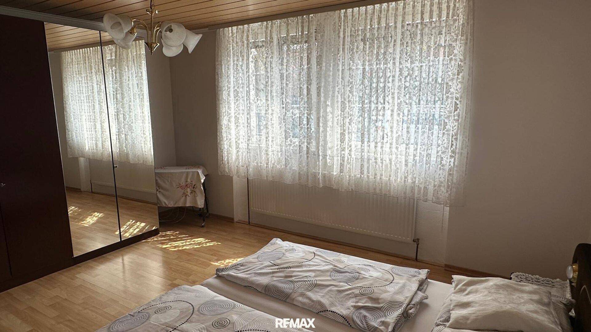Helles Schlafzimmer mit Spiegelschränken, Holzboden und großen Fenstern.
