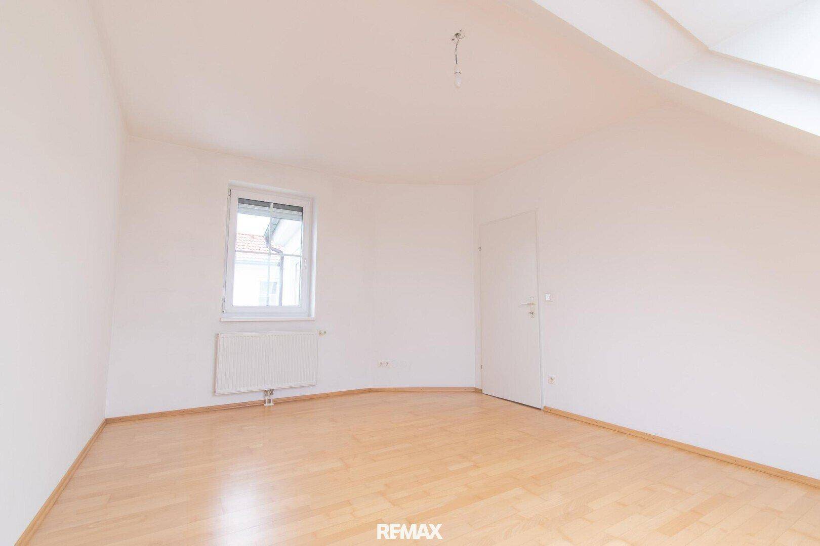Leeres Schlafzimmer mit hellem Parkettboden, Fenster und Dachschräge.