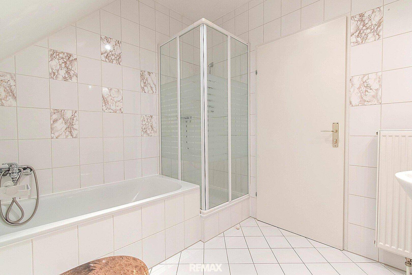 Badezimmer mit Badewanne, Duschkabine und weißen Fliesen im Dachgeschoss.