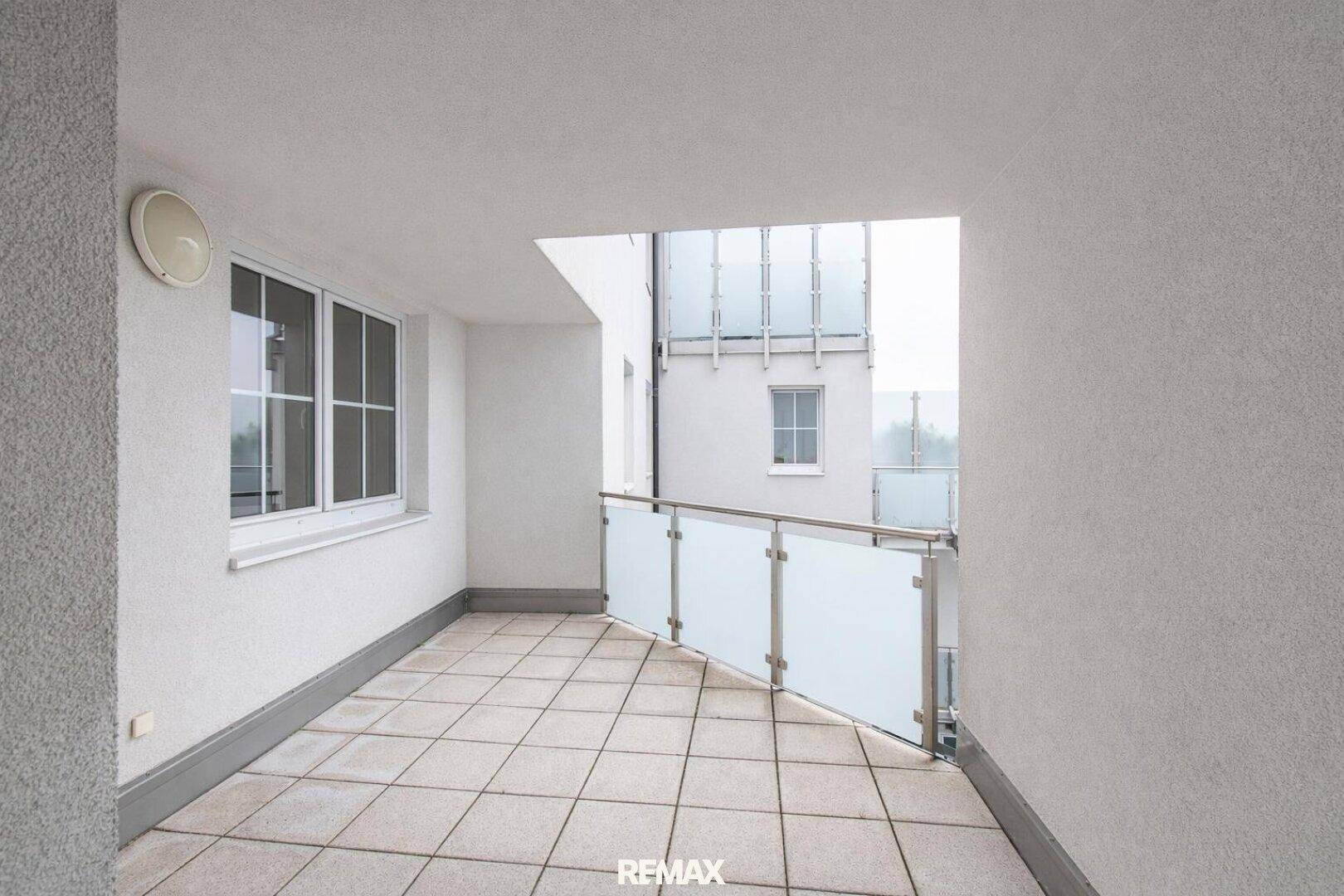 Geräumiger Balkon mit Fliesenboden und Glasgeländer, ideal für Entspannung im Freien.