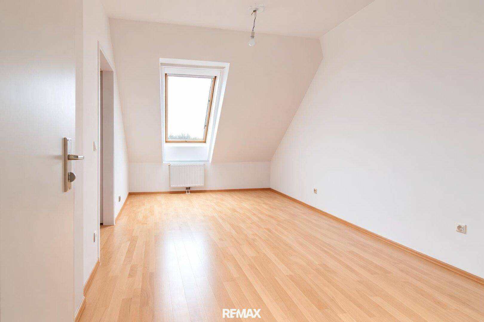 Helles, leeres Schlafzimmer im Dachgeschoss mit Dachfenster und Parkettboden.