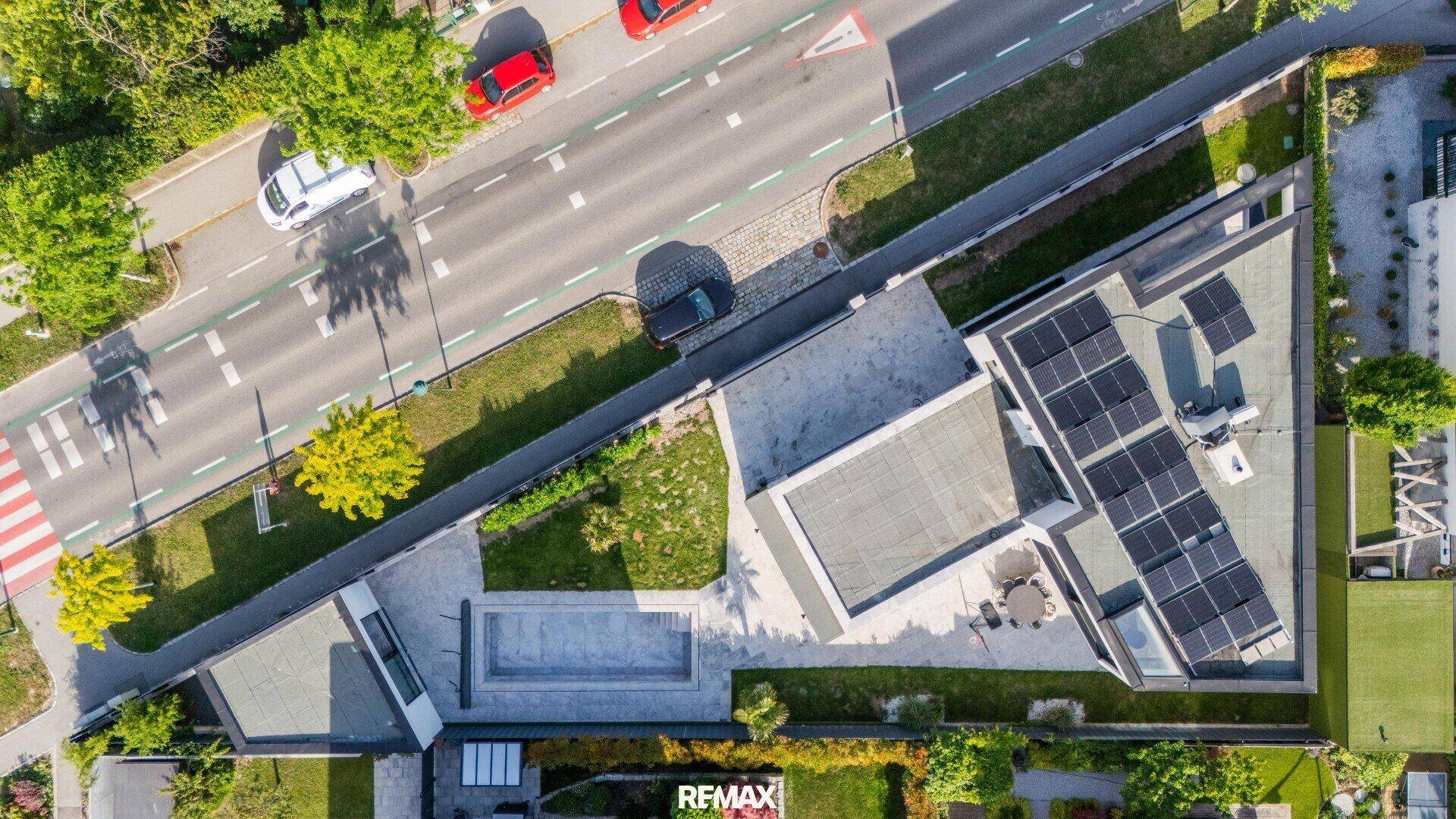 Vogelperspektive des Anwesens mit Solaranlage auf dem Dach, Pool und Straße.
