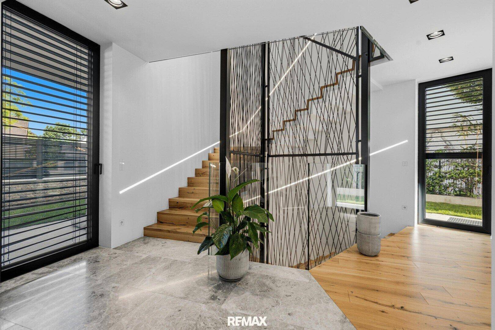 Eingangsbereich mit moderner Holztreppe, dekorativem Geländer und großen Fenstern.