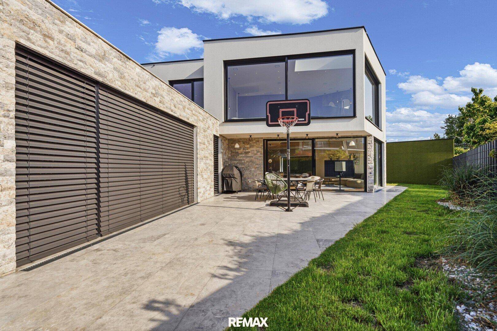 Rückansicht des modernen Hauses mit Terrasse, großen Fenstern und Basketballkorb.