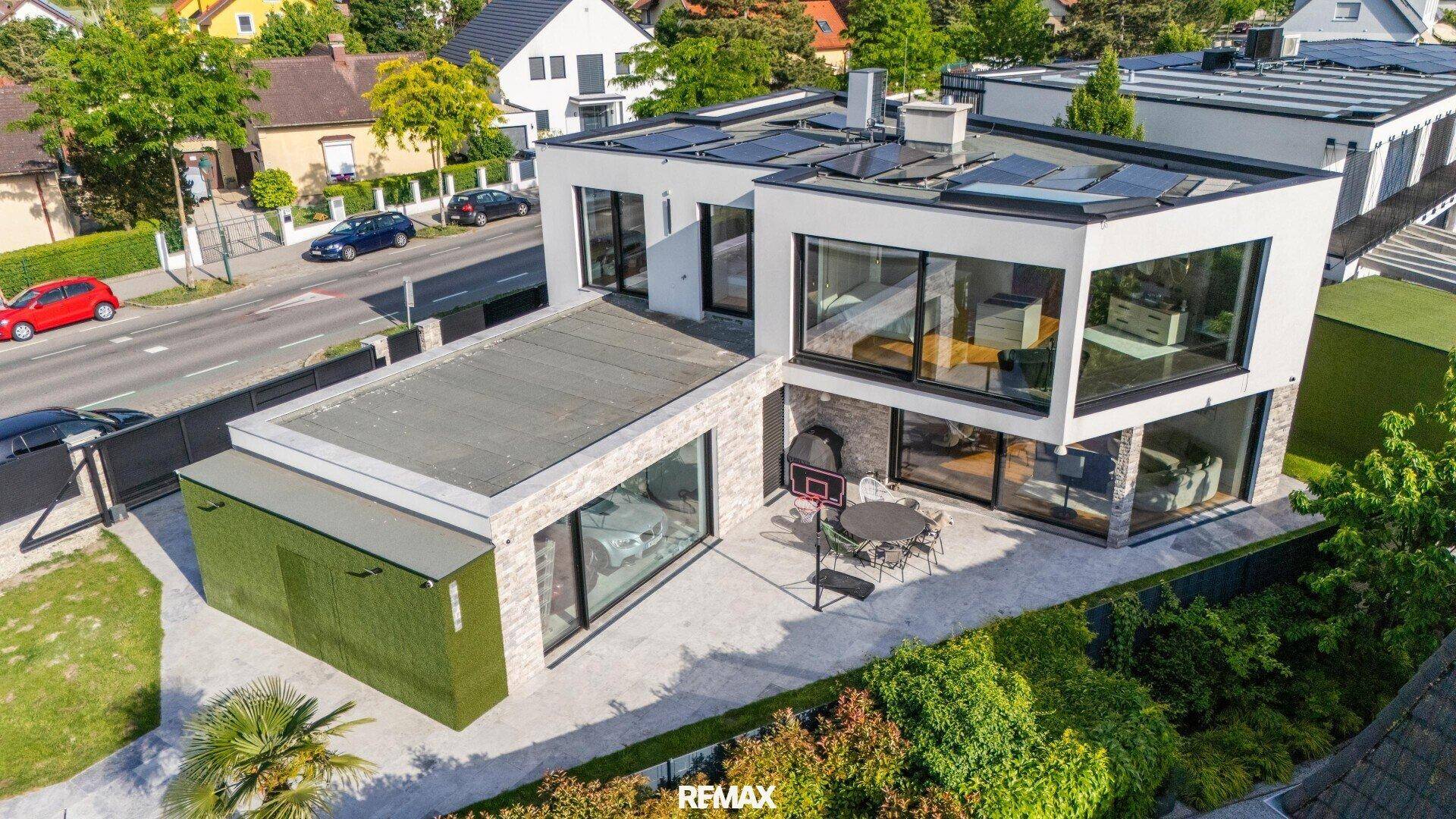 Moderne Villa von oben mit Flachdach, großen Fenstern und gepflegtem Garten.