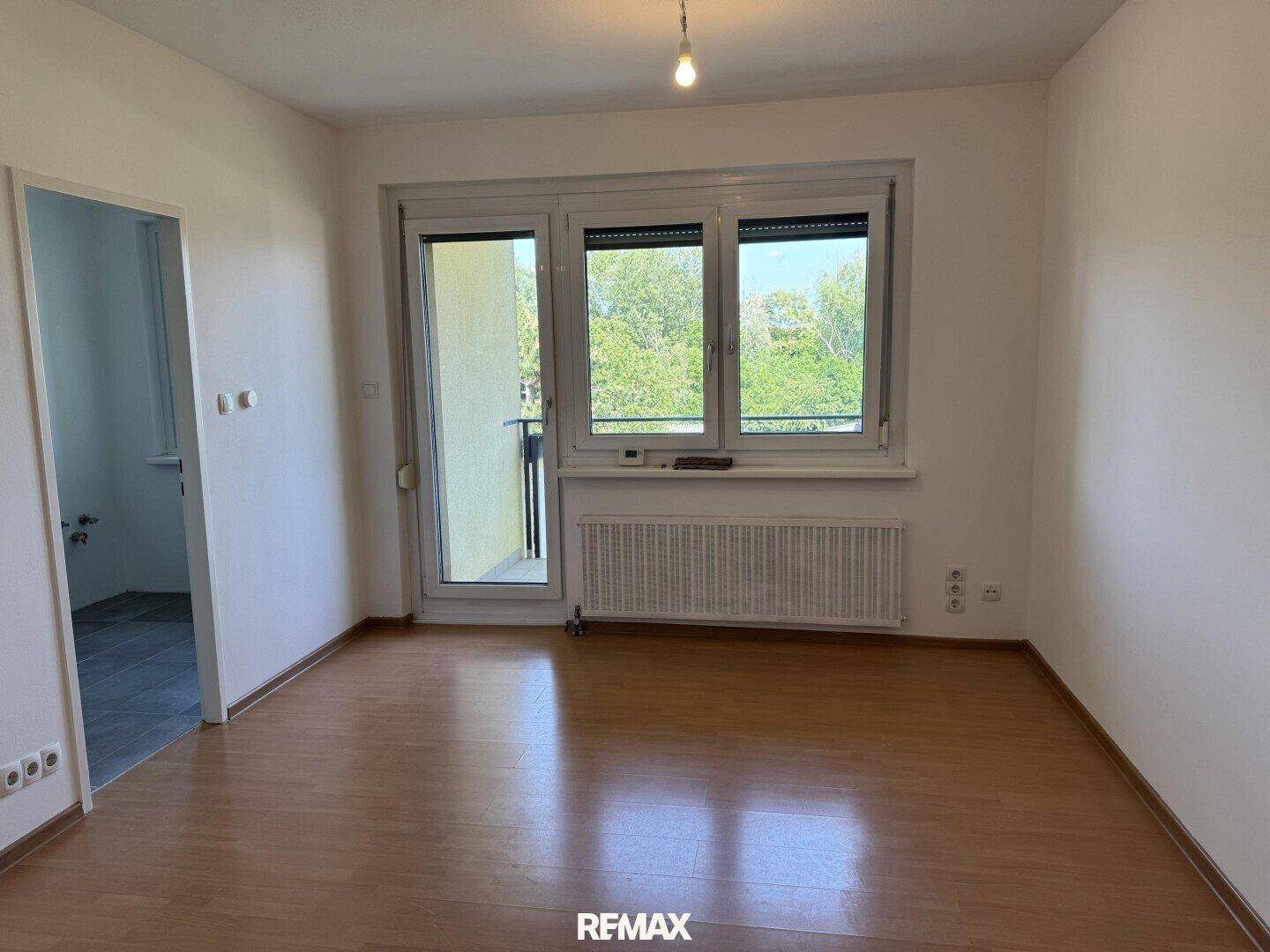 Heller, leerer Raum mit Holzboden und Zugang zu einem Balkon durch eine große Fenstertür.