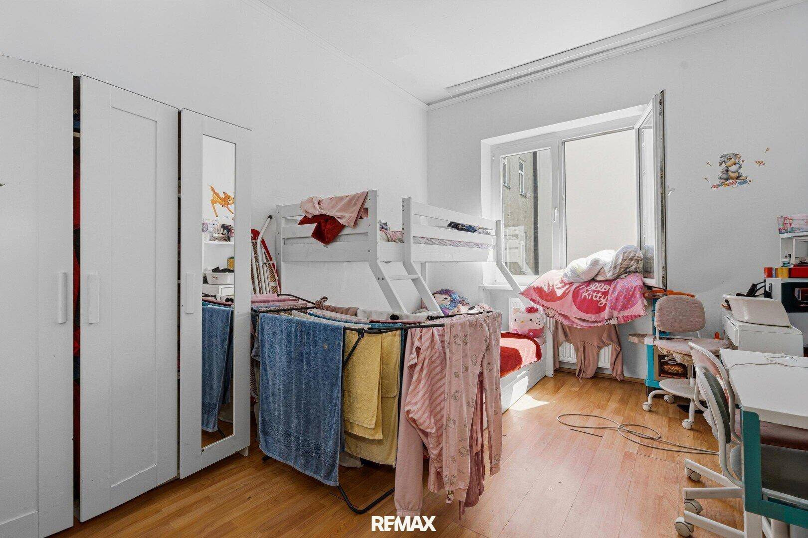 Helles Kinderzimmer mit Etagenbett, Kleiderschrank und Fenster.