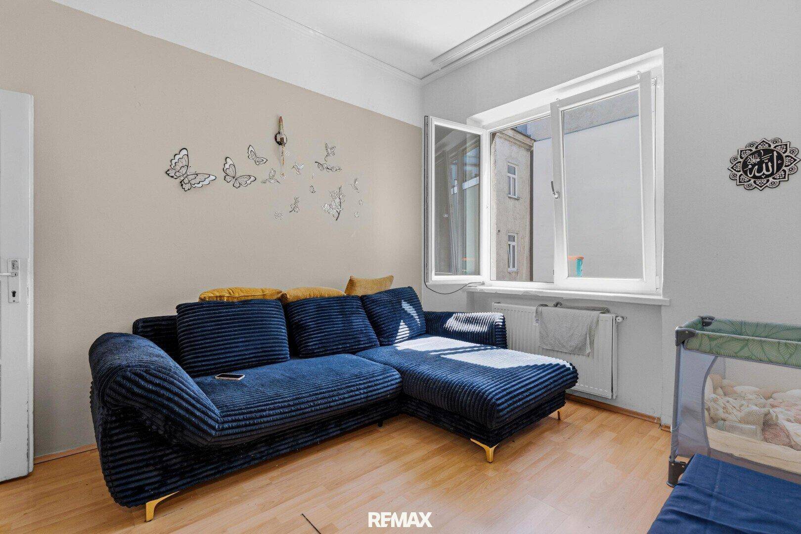 Wohnzimmer mit einem bequemen blauen Ecksofa und einem großen Fenster.