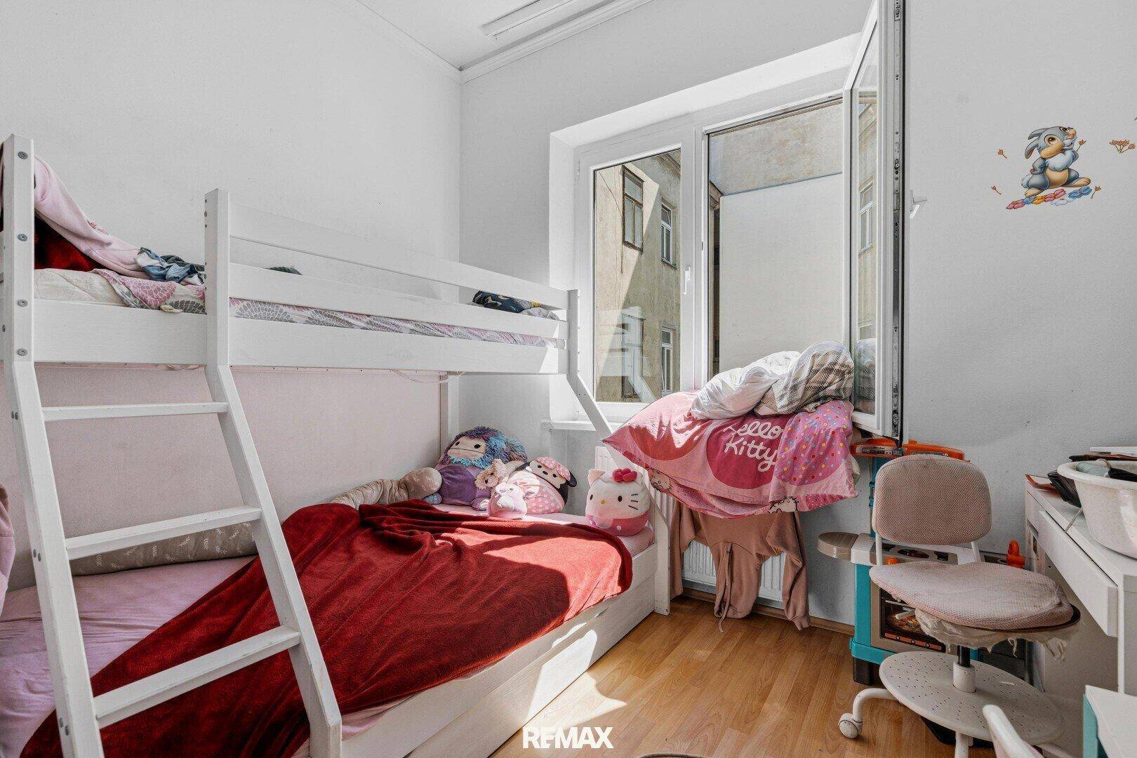 Kinderzimmer mit Etagenbett, Schreibtisch und Fenster, das Tageslicht hereinlässt.