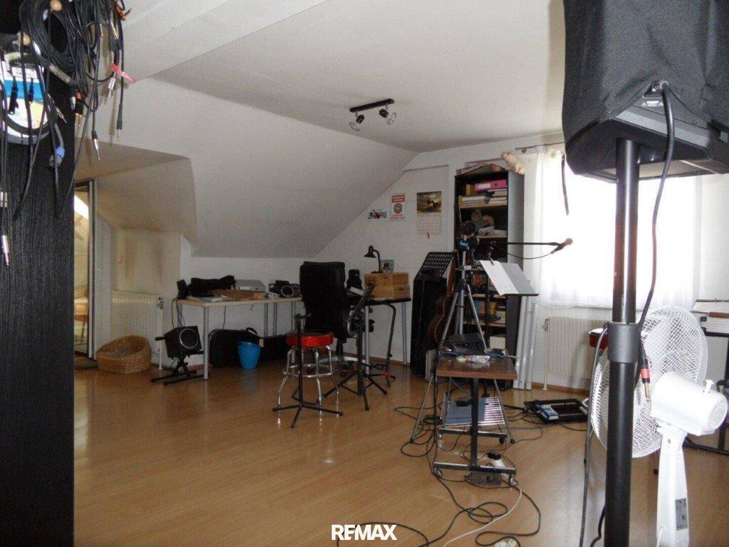 Dachgeschossraum mit schrägen Wänden, eingerichtet als Musik- oder Medienzimmer mit Holzboden.