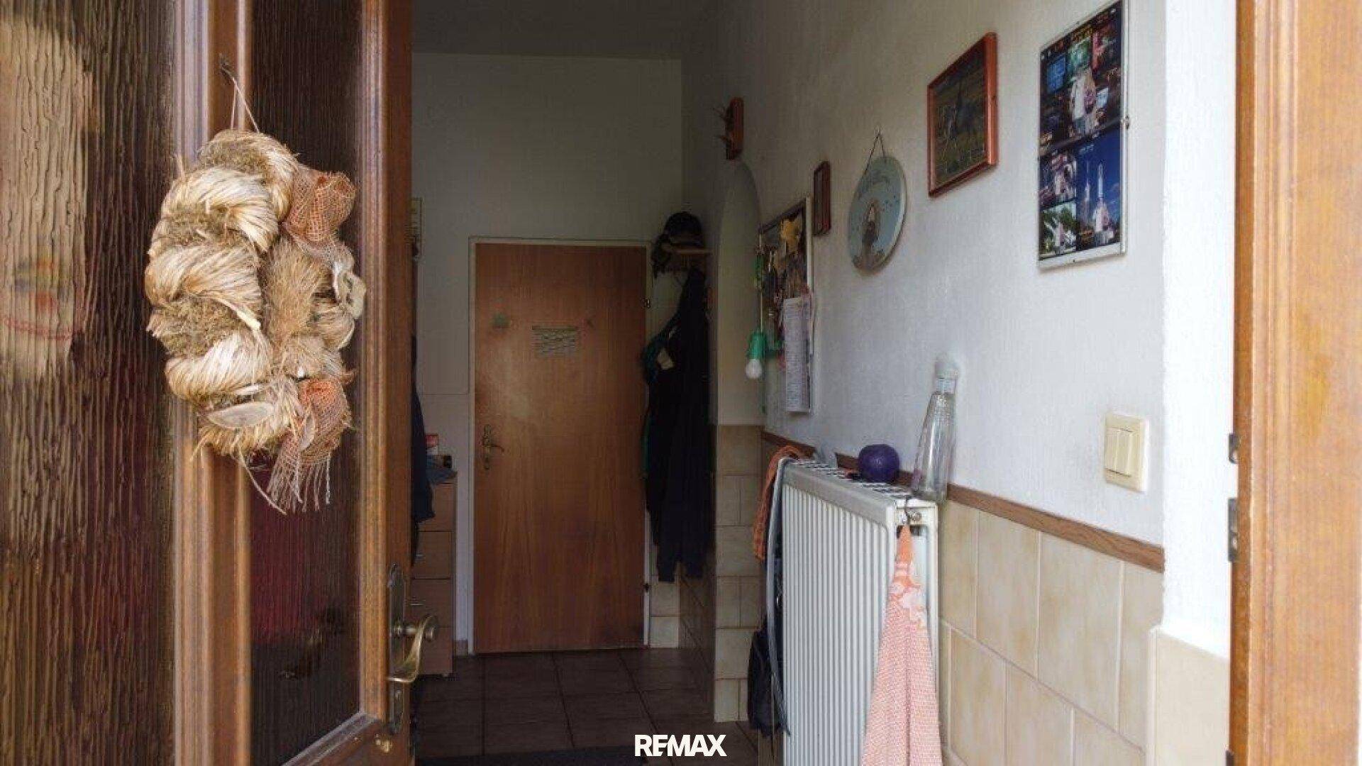 Eingangsbereich mit Fliesenboden, Heizkörper und einer Holztür, hell beleuchtet.