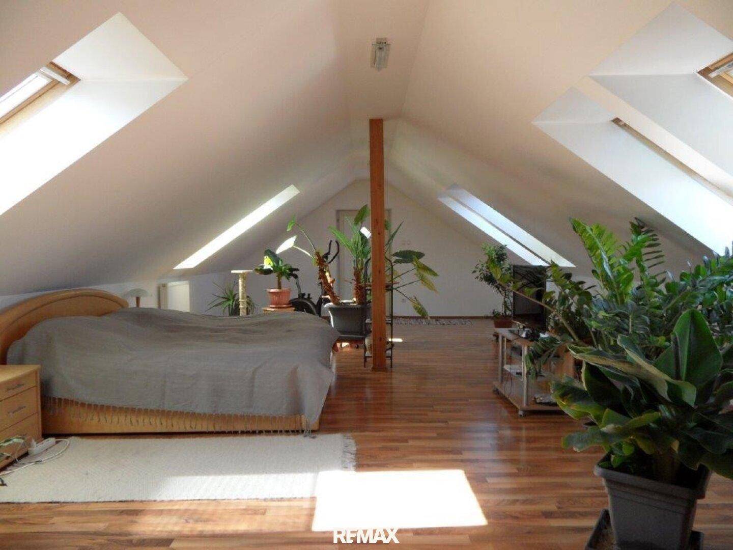 Helles Schlafzimmer im Dachgeschoss mit schrägen Wänden, Dachfenstern und Holzboden.